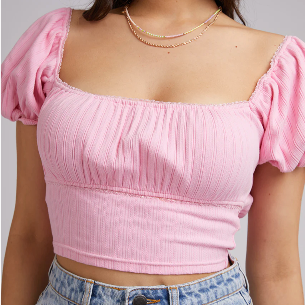 Pink crop top with puffed sleeves worn by a person on a white background
