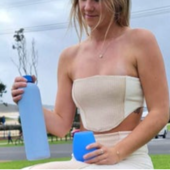Woman holding two blue bottles outdoors with a blurred background