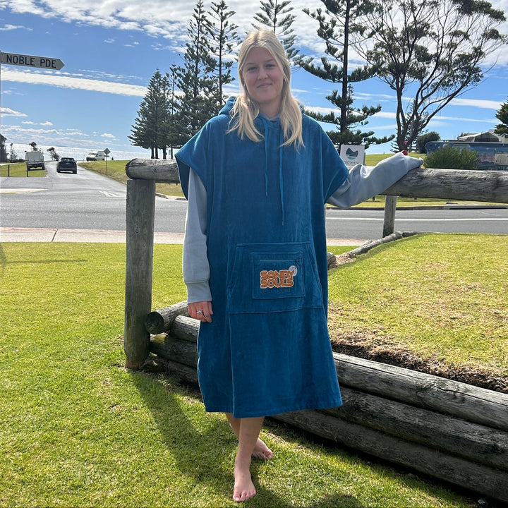 Person wearing a blue hooded poncho standing outdoors with grass and trees in the background