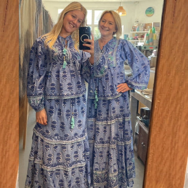 Woman taking a mirror selfie wearing a blue patterned dress in a room.