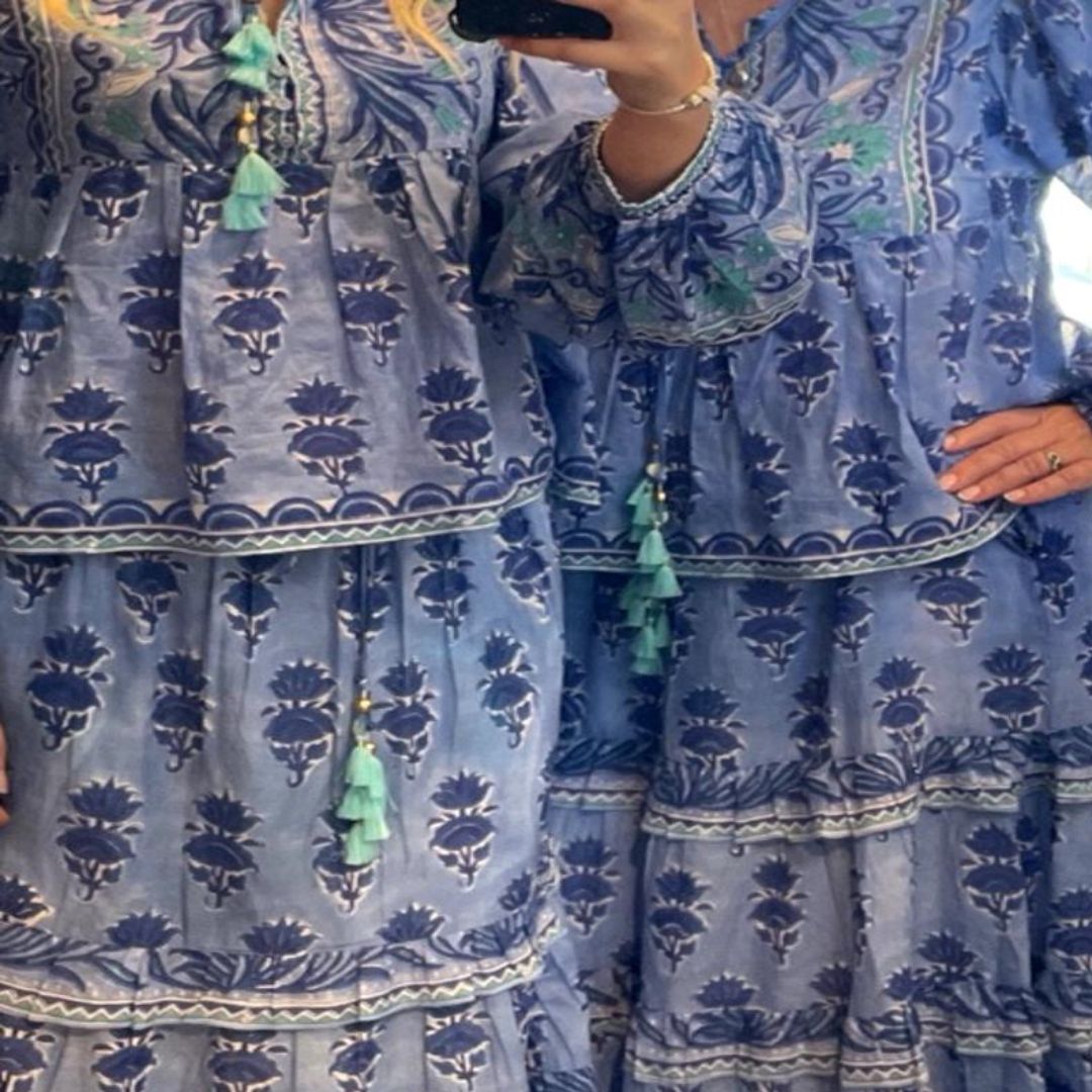 Person wearing a blue patterned dress with green tassels in front of a mirror.