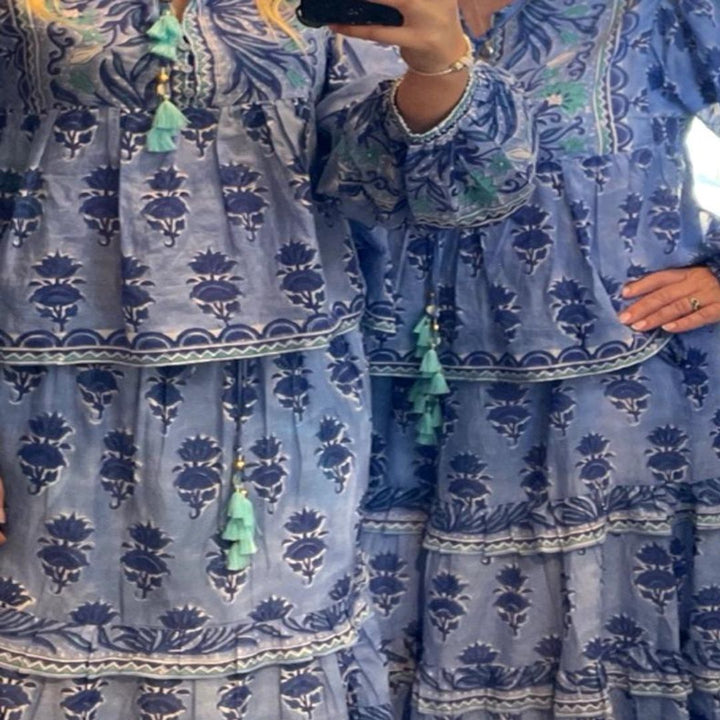 Person wearing a blue patterned dress with green tassels in front of a mirror.