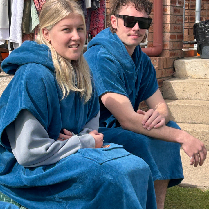 Two people sitting outdoors wearing blue hooded towels.