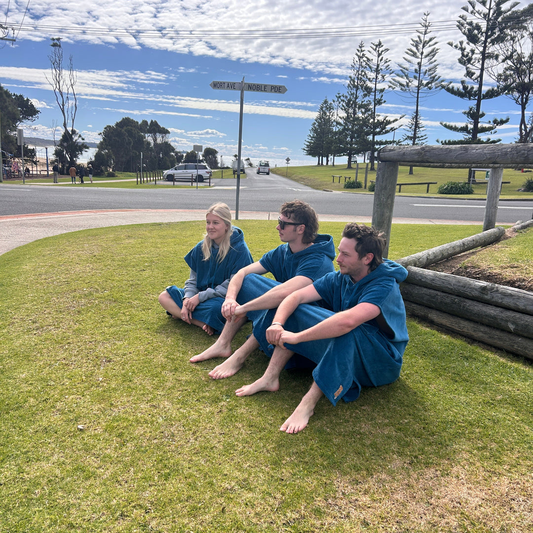 Two children in blue outfits sitting on grass by a road with trees in the background