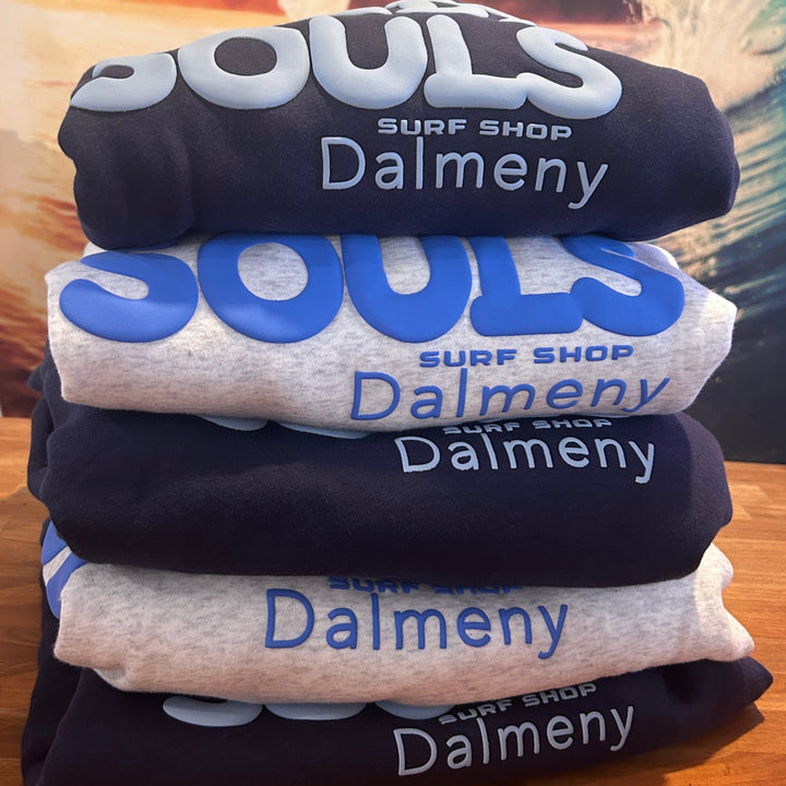 Bench with folded pile of grey and navy hooded jumpers with blue Sandy souls surf shop Dalmeny printed on