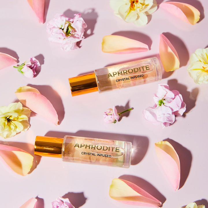 Two 'Aphrodite' crystal-infused products on a pink background with flowers.