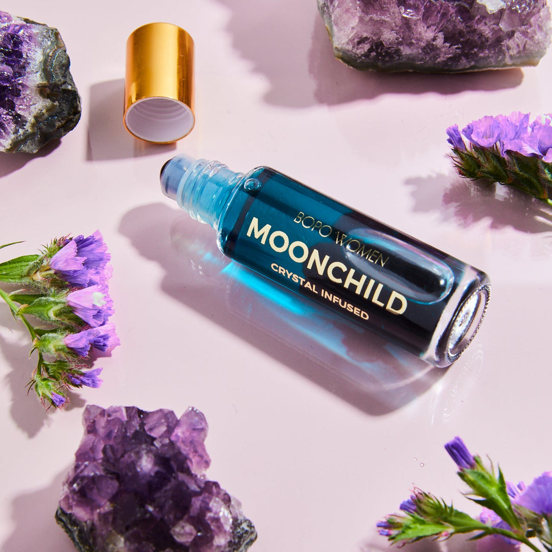 Bottle of 'MOONCHILD' crystal-infused product on a light pink background with purple crystals and flowers.