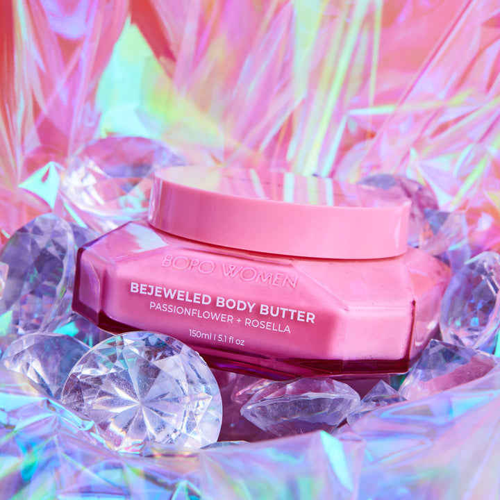 Pink body butter jar with 'Bejeweled Body Butter' text on a colorful, gemstone-studded background.