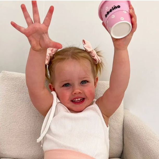 Child holding a pink cup with 'Bebé' text, sitting on a couch.