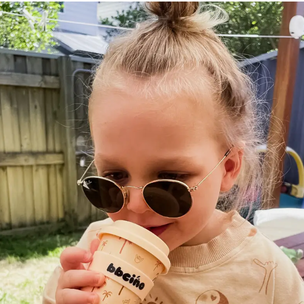 Child wearing sunglasses and holding a coffee cup outdoors