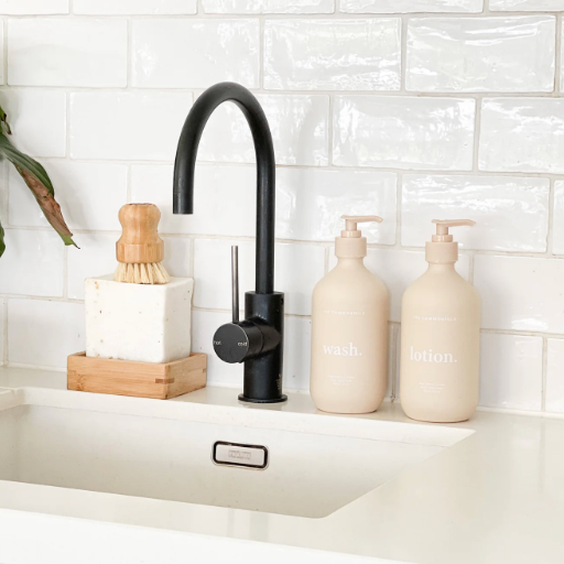Black faucet with beige soap dispensers on a kitchen sink against a white tiled wall.