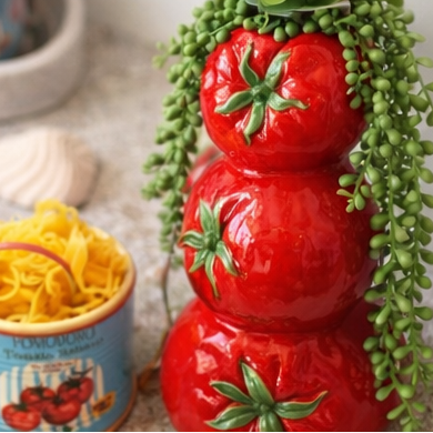 Decorative tomato-themed ceramic pots with a candle and decorative items on a wooden surface.